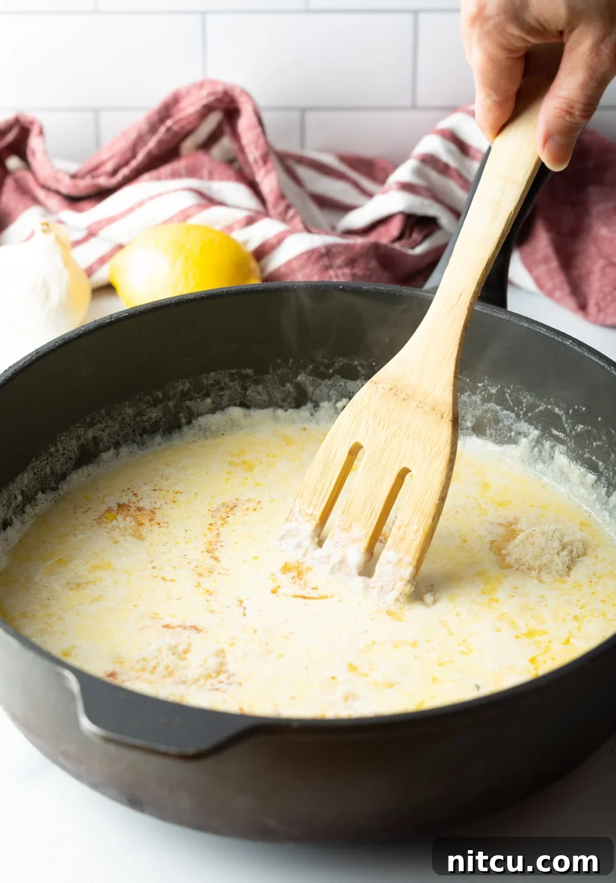 Fettuccine pasta being expertly tossed in a large skillet with creamy Alfredo sauce