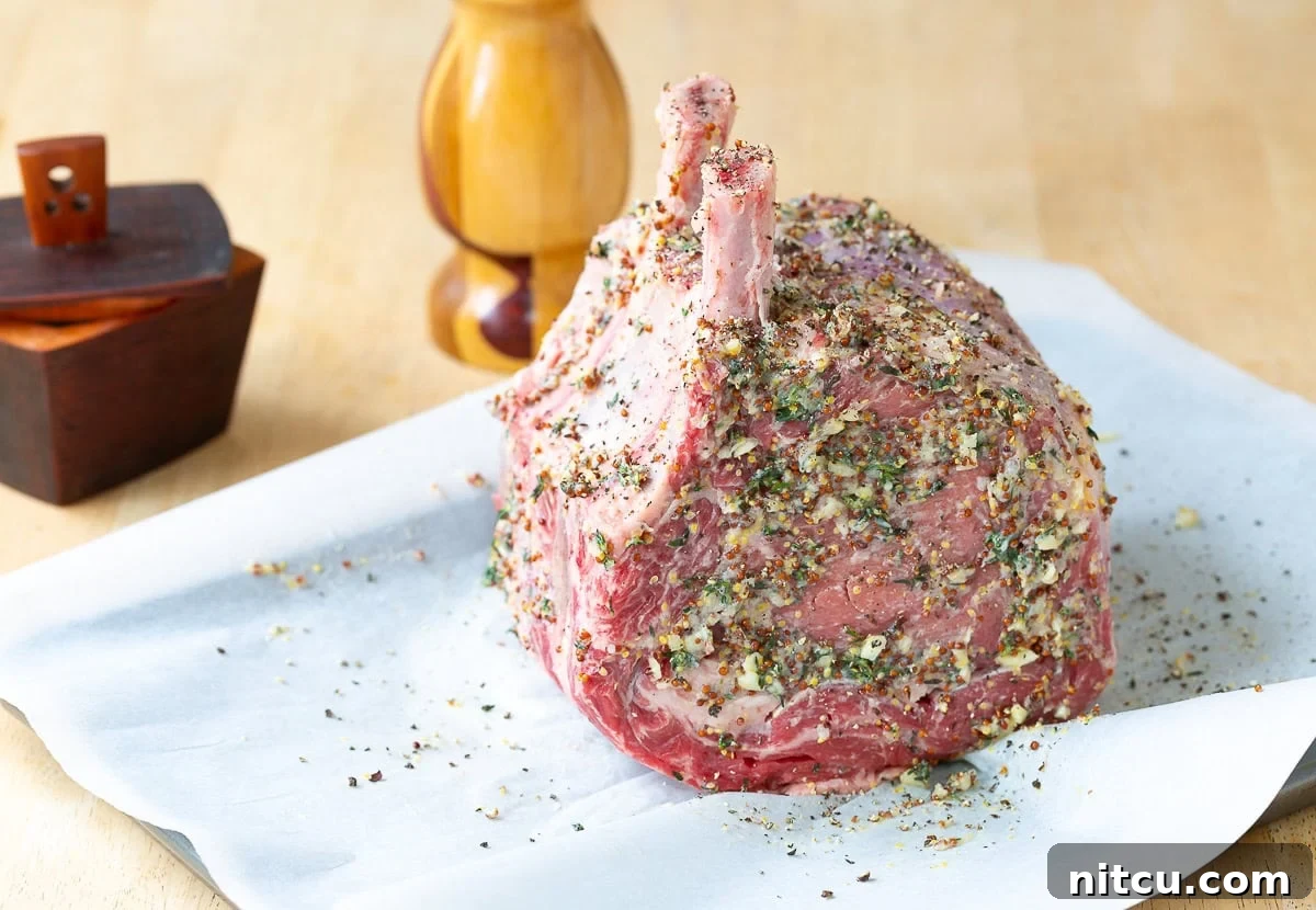 The standing rib roast is generously covered in a fragrant herb and mustard marinade, prepared for roasting.