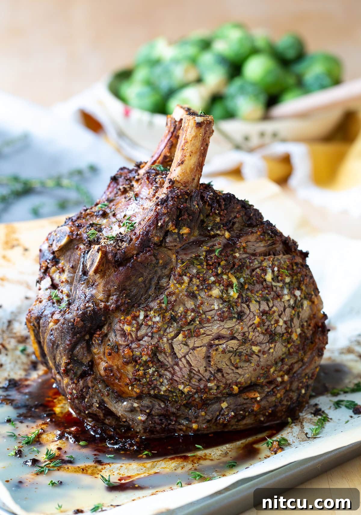 A close-up side shot of the crispy herb crust of the prime rib, with savory au jus pooled on the baking tray.