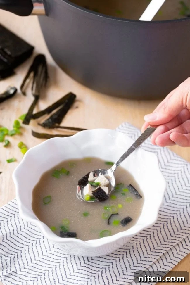Side view of a pot and bowl filled with homemade Japanese Miso Soup, accompanied by a wooden spoon.