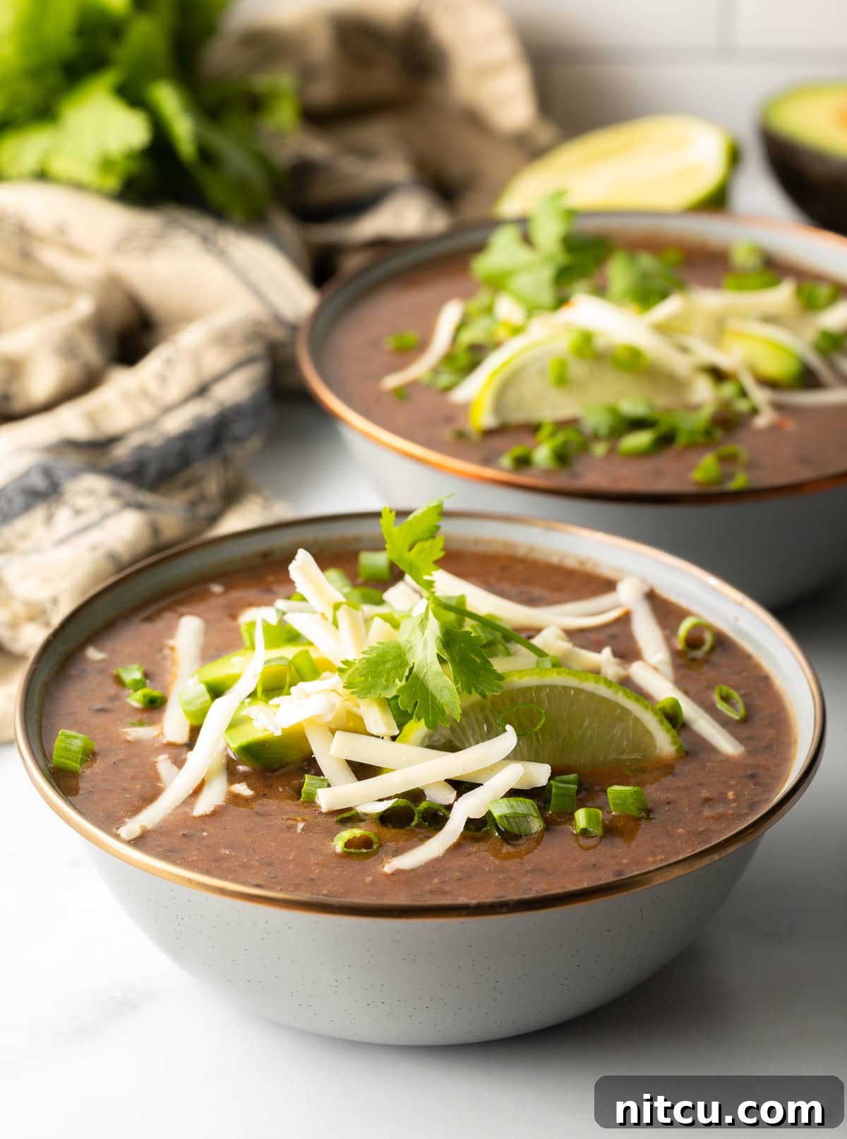 Slow cooker black bean soup in a gray bowl with fresh garnishes, showcasing a rich, dark color and vibrant toppings.