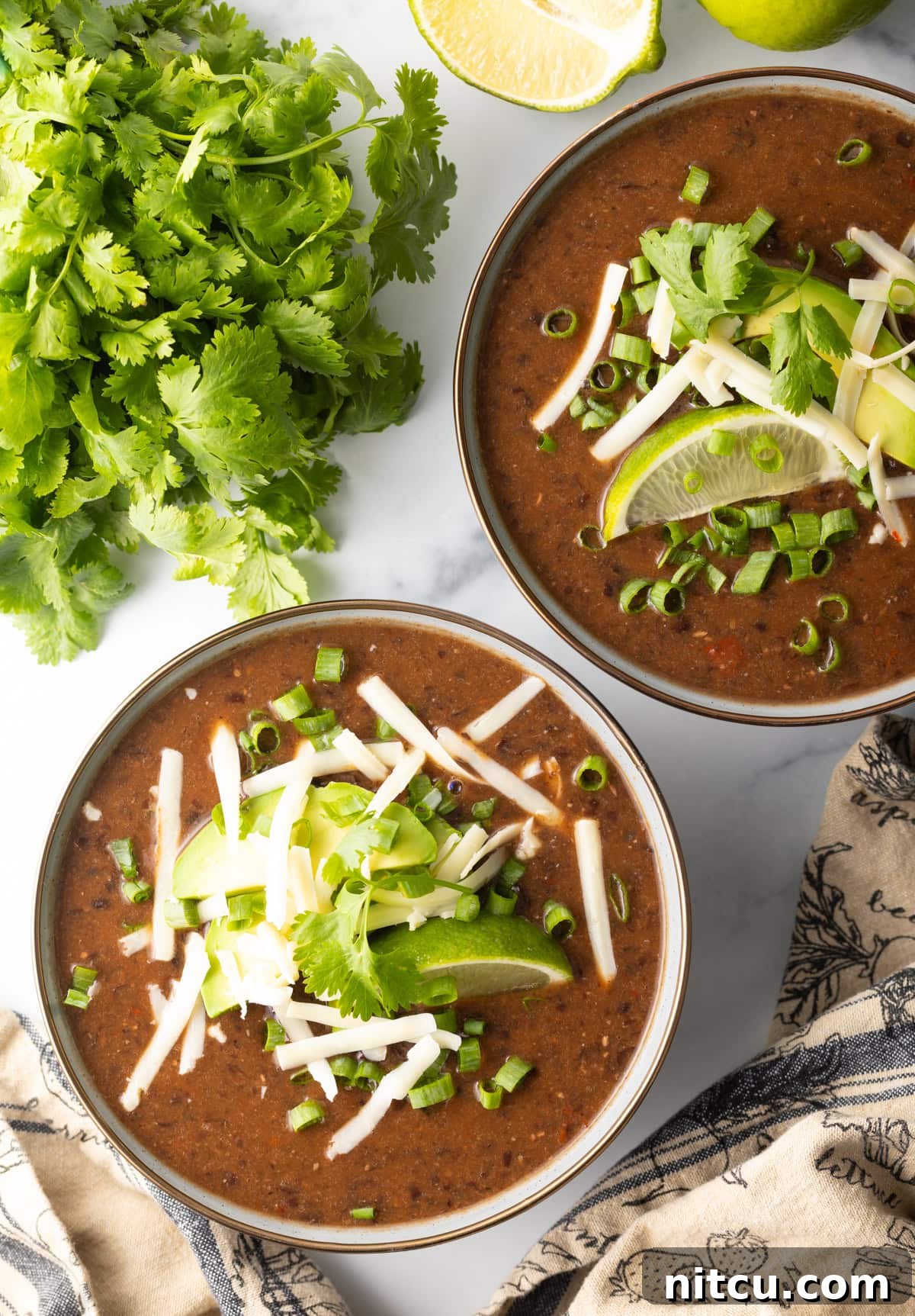 Top down view of two bowls filled with black bean soup, garnished with fresh herbs and a swirl of cream.