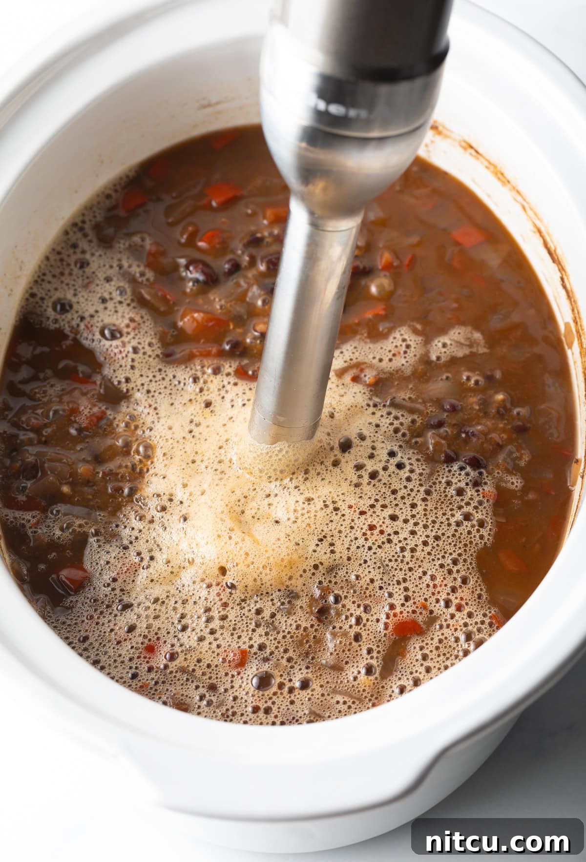Immersion blender mixing black bean soup in a slow cooker, creating a creamy texture.
