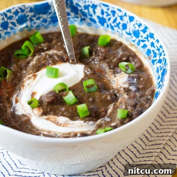 Closeup of a bowl of black bean soup topped with sour cream and chopped scallions, highlighting the fresh garnishes.
