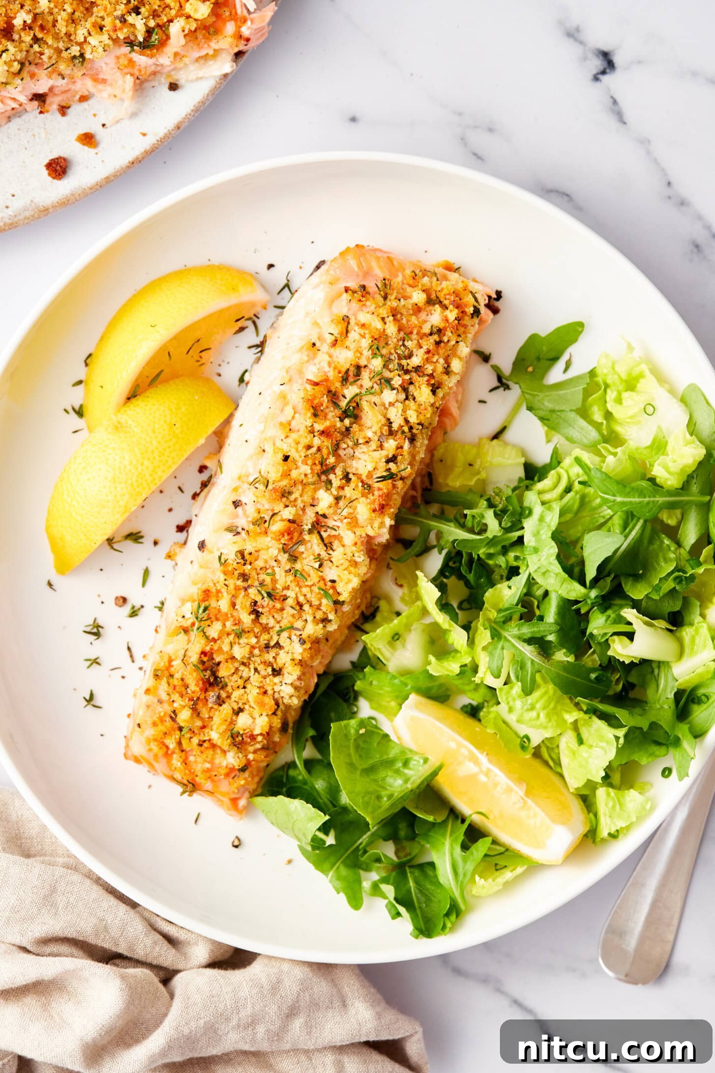 Two pieces of oven baked salmon adorned with a savory parmesan herb crust, resting on a parchment-lined baking sheet, with a spatula nearby.