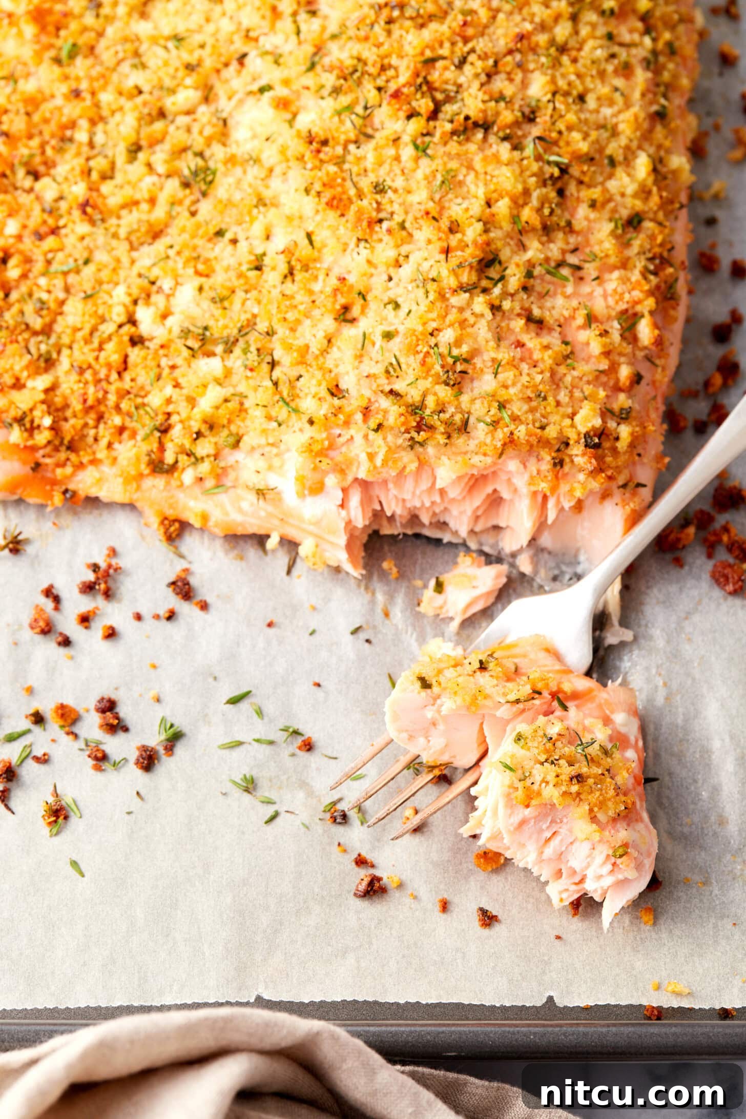 A fork gently removing a piece of perfectly cooked, flaky parmesan crusted salmon, revealing its tender interior.