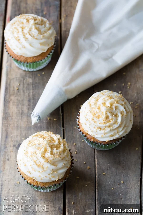 A piping bag filled with creamy frosting next to a selection of freshly decorated hummingbird cupcakes.