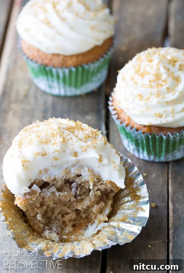 A delightful Hummingbird cupcake with a large bite taken out, revealing its moist interior packed with fruit and nuts.