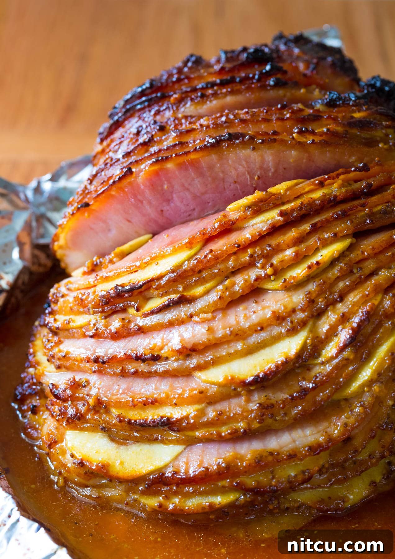 A beautifully roasted spiral cut ham, with vibrant apple slices tucked between each cut, and a glistening honey mustard glaze coating its surface, ready to be served as a festive holiday centerpiece.