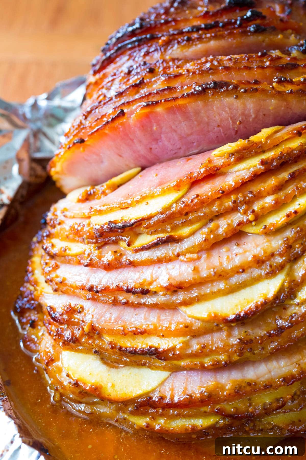 A vibrant close-up of the spiral ham showing the meticulously tucked apple slices and the rich, golden-brown glaze, ready to be carved.
