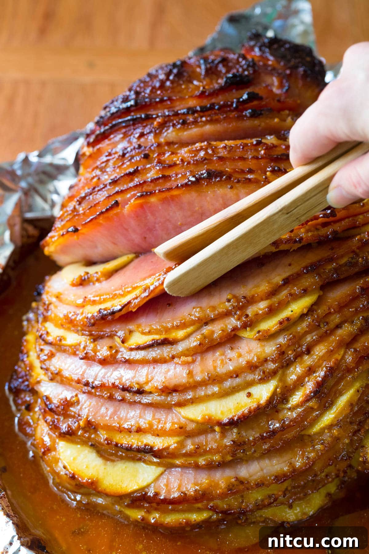 Tongs gracefully selecting a slice of the apple-stuffed baked ham from the serving platter, highlighting its readiness to be enjoyed.