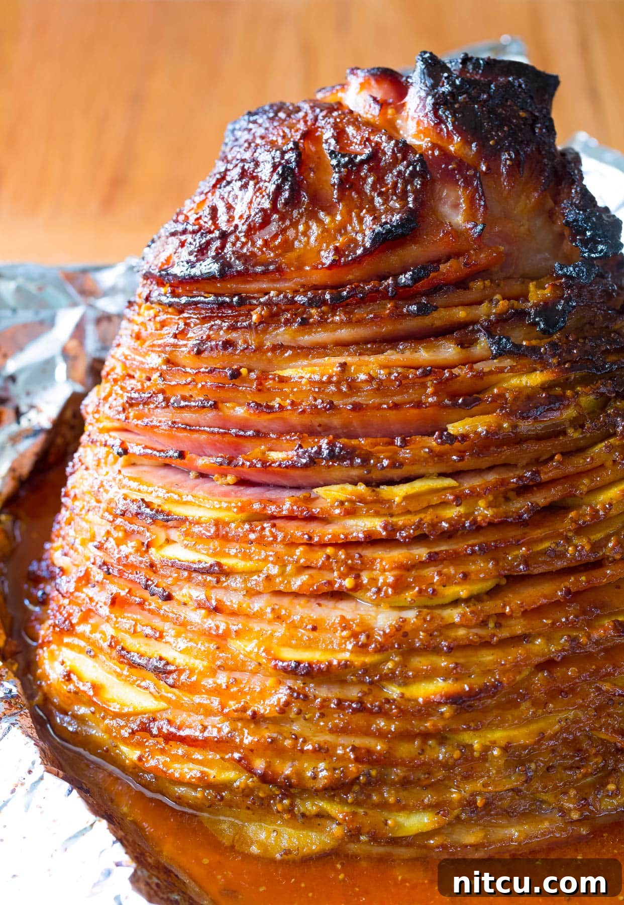 A close-up shot of the baked ham with apples nestled in a baking tray, showing the rich, golden-brown glaze and tender apple slices.