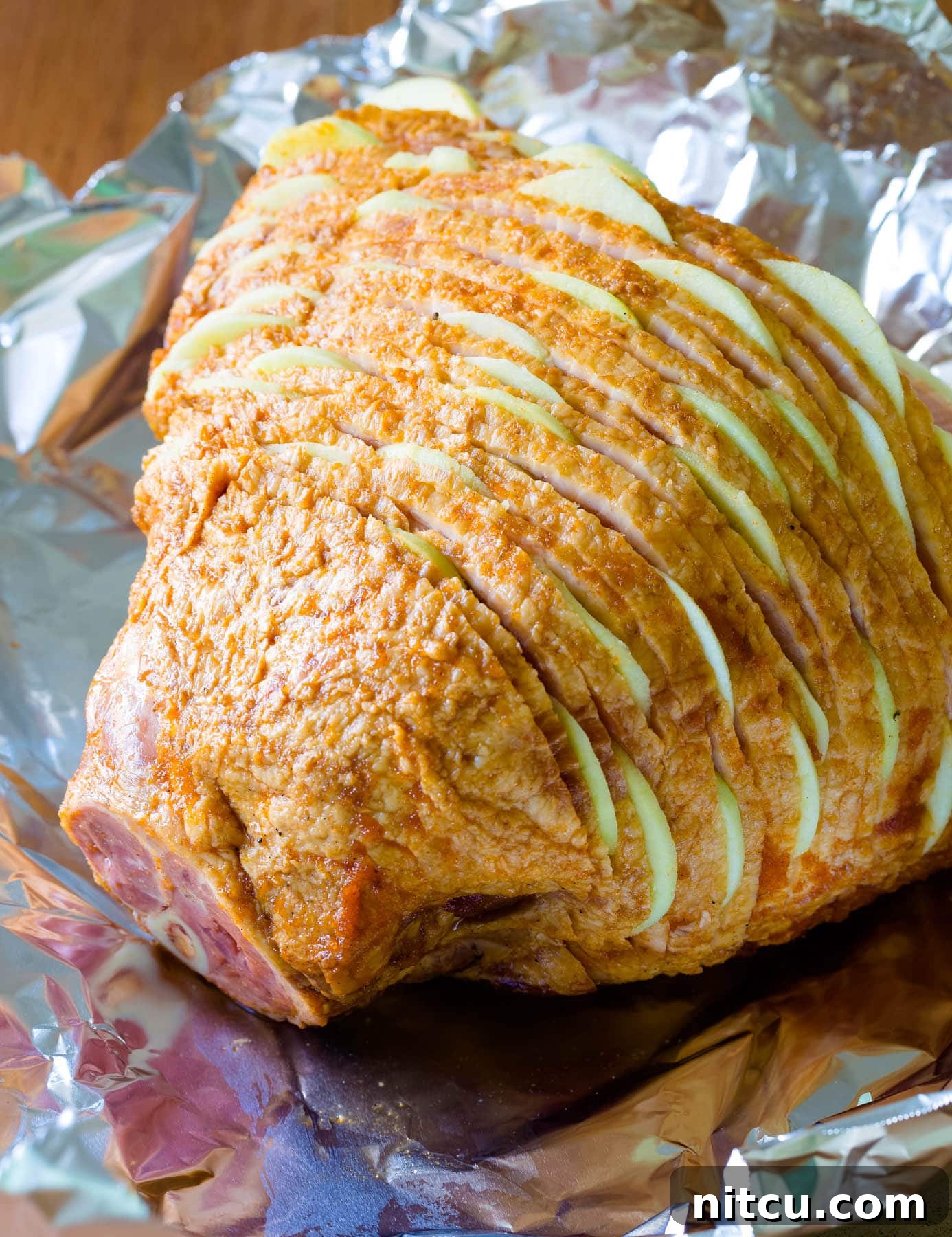 A spiral ham beautifully stuffed with thin slices of Granny Smith apples between each cut, ready for glazing and baking.