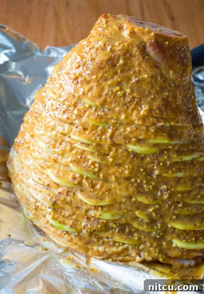 The spiral ham, already partially glazed, resting on a baking sheet, ready to go into the oven.