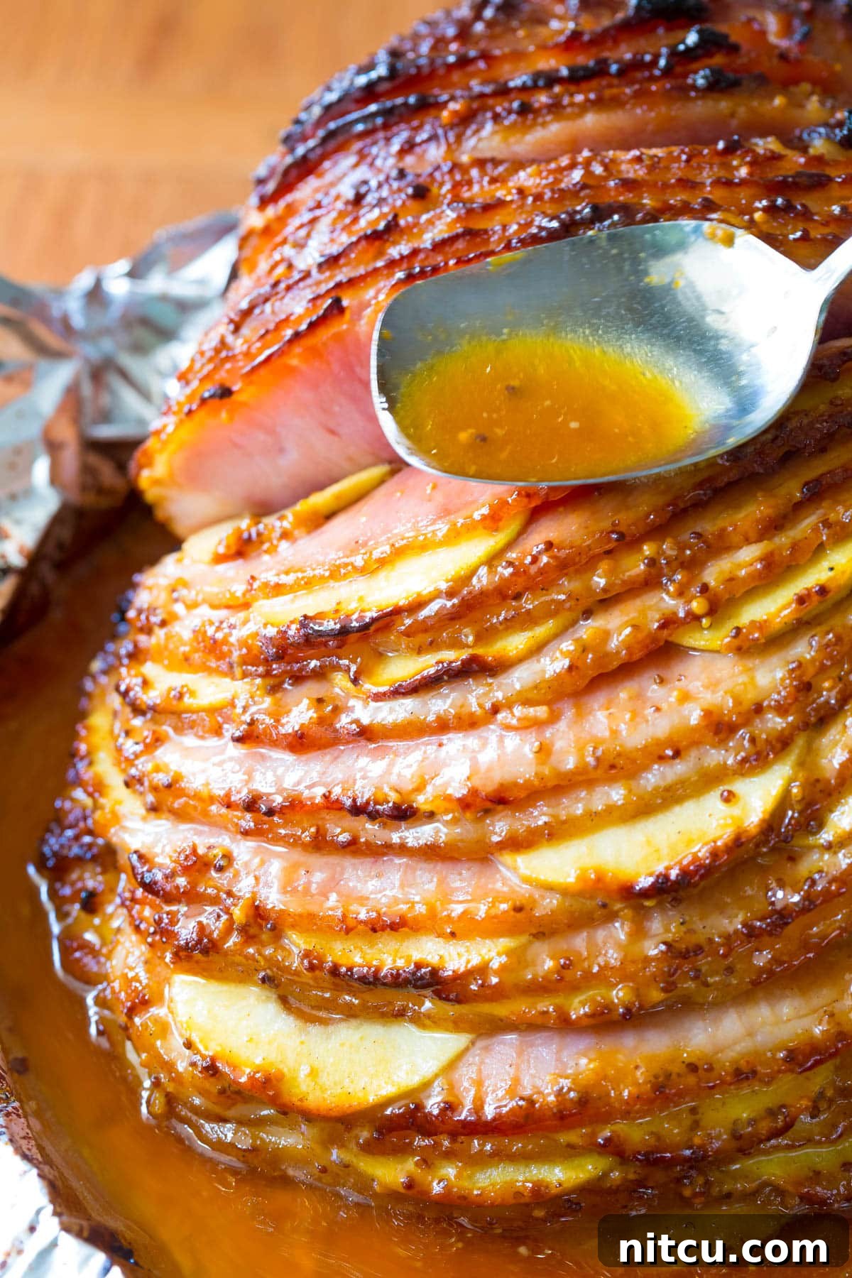 The fully baked honey mustard glazed ham, glistening and caramelized, nestled among softened apple slices in the baking dish.