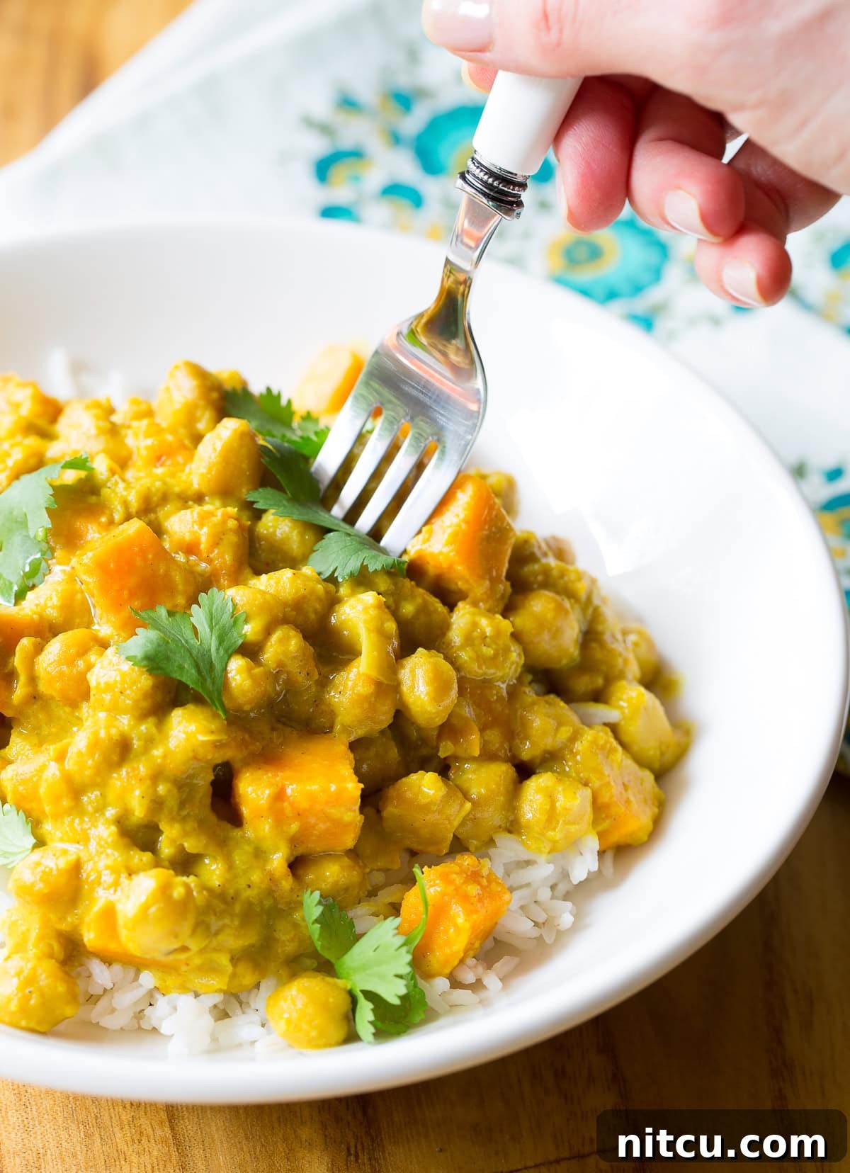 A fork digging into a plate full of crockpot chickpea curry, showing the creamy texture and whole ingredients.