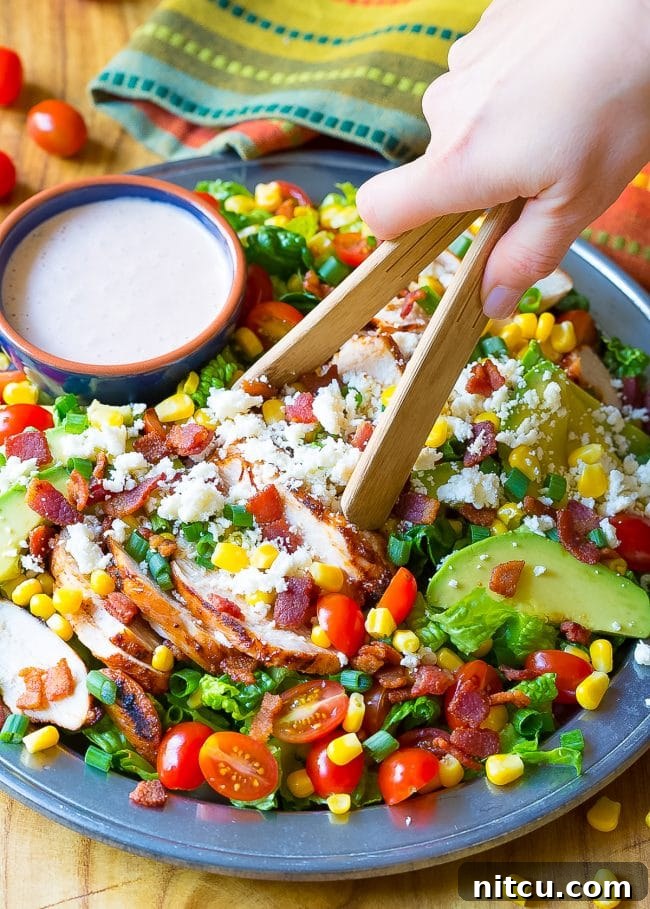 Hand is tossing the Mexican chicken salad in a bowl with wooden tongs. 