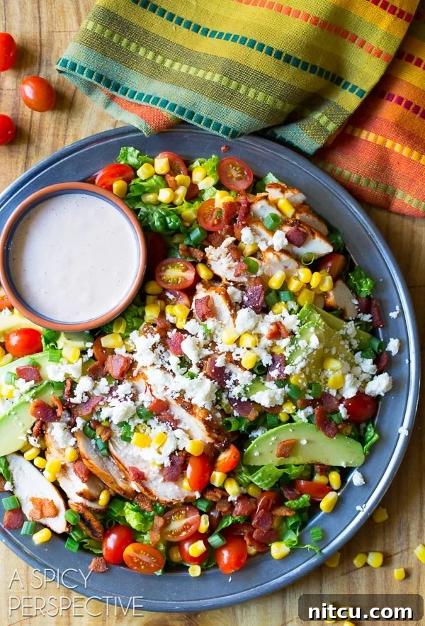 Overhead shot of large platter filled with completed Mexican grilled chicken salad and a ramekin filled with dressing. 