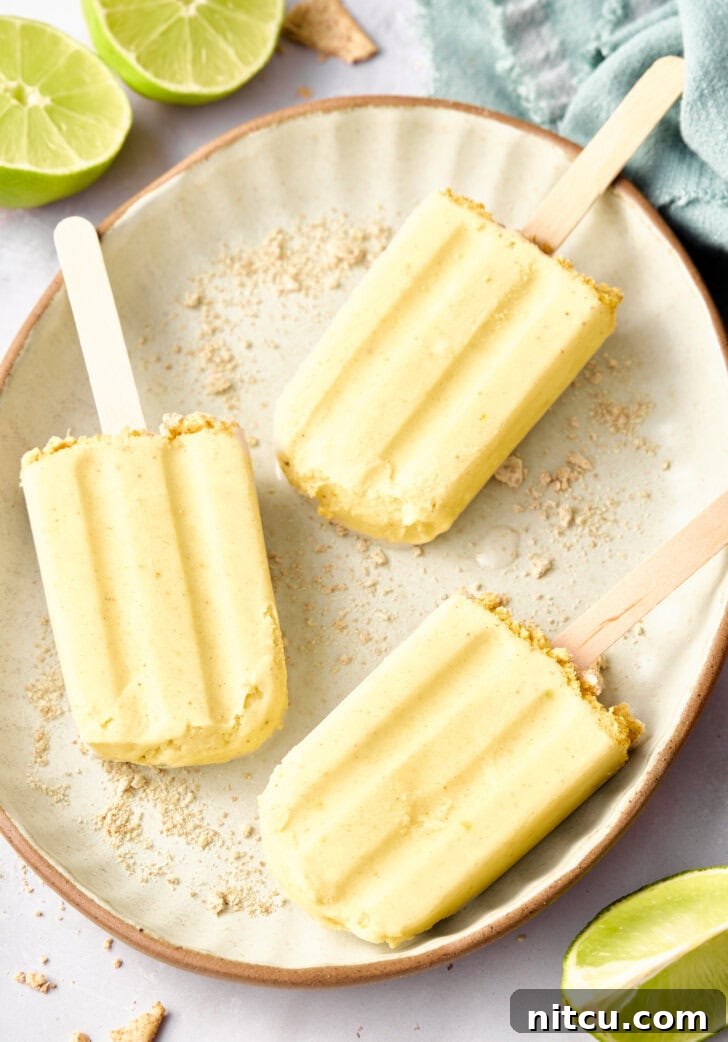 Key Lime Pudding Popsicles - lime popsicles on a plate with graham cracker crust garnish and limes around