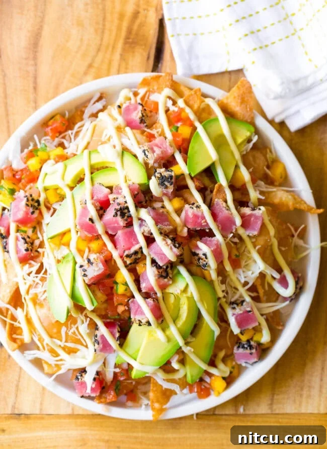 Ahi tuna nachos overhead view, white bowl loaded with crispy wonton chips, cubes of seared ahi tuna, mango pico de gallo, shredded cabbage, avocado slices, and a drizzle of wasabi mayo.