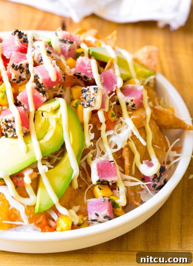 White bowl loaded with crispy wonton chips, cubes of seared ahi poke, mango pico de gallo, shredded cabbage, avocado slices, and a drizzle of wasabi mayo.