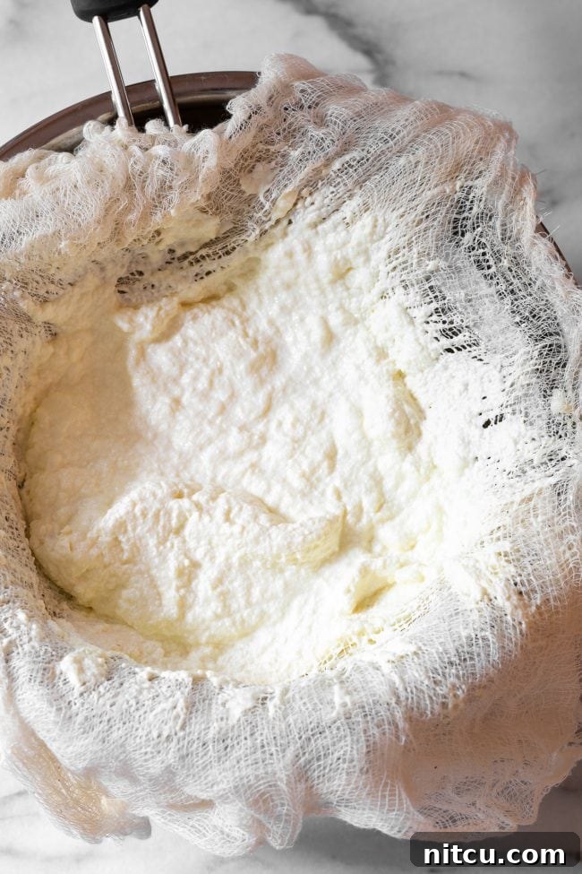 Rich, creamy ricotta cheese curds collected on a cheesecloth, resting over a metal bowl, illustrating the separation of curds from whey.