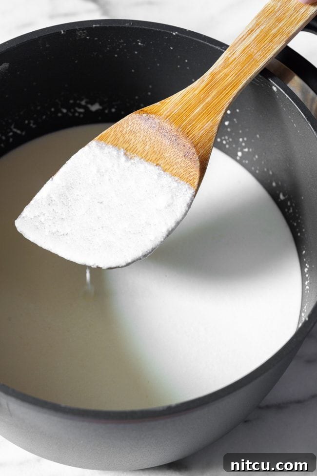 Stirring the milk and cream mixture gently with a wooden spoon in a metal pot over heat, ensuring even heating.