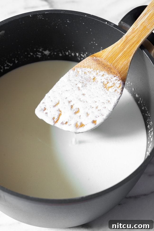 A wooden spatula showing a thin coating of early curds over the cooking ricotta mixture in a large black pot, indicating the milk is beginning to curdle.