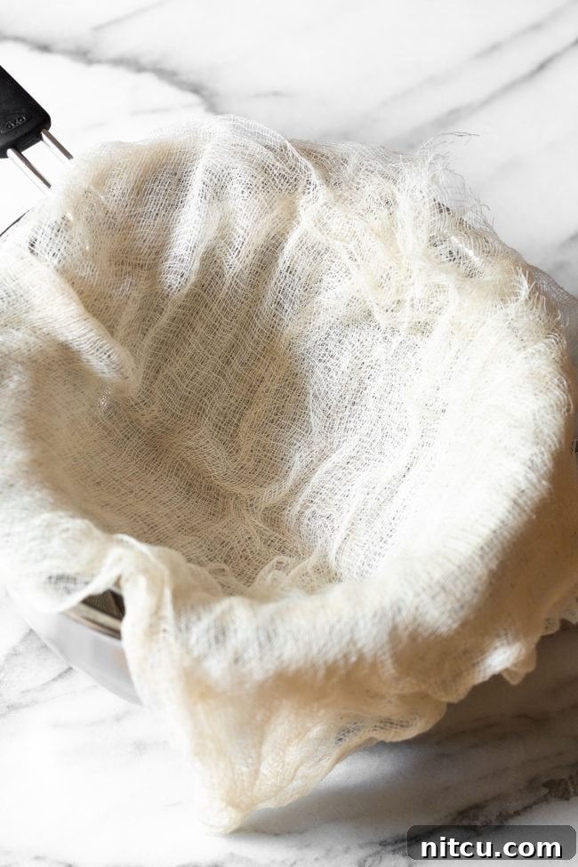 A clean cheesecloth meticulously laid over a fine-mesh sieve, which is placed atop a metal bowl, preparing for the straining process.