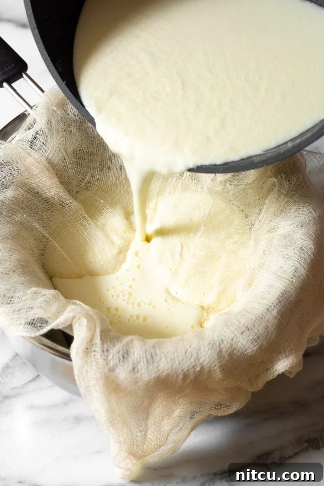 Carefully pouring the curdled milk mixture into the cheesecloth-lined sieve, initiating the separation of creamy curds from clear whey.