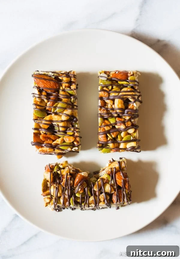 Top down view of three homemade paleo nut bars with chocolate drizzle on a pristine white plate, showcasing their inviting texture and rich topping.