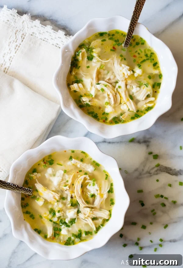An inviting overhead shot of two bowls of Greek lemon chicken soup, garnished with fresh herbs and lemon wedges, on a rustic wooden table.