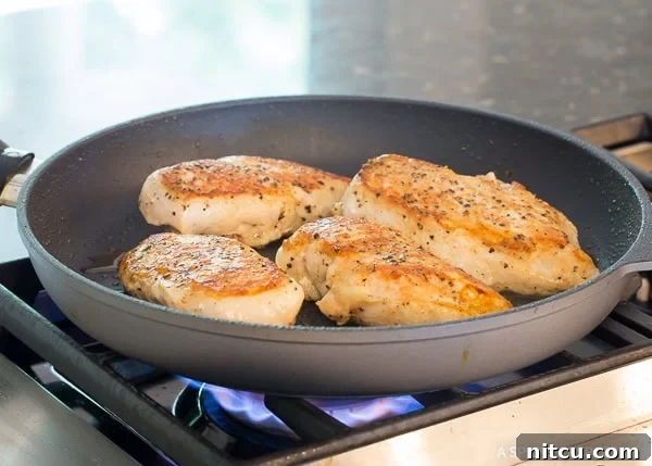 Chicken breast being seared in a cast iron skillet, acquiring a golden crust.