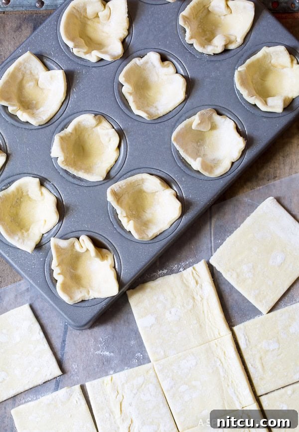 Making Mini Pumpkin Pies with love and precision. Hands pressing puff pastry into mini muffin tins.