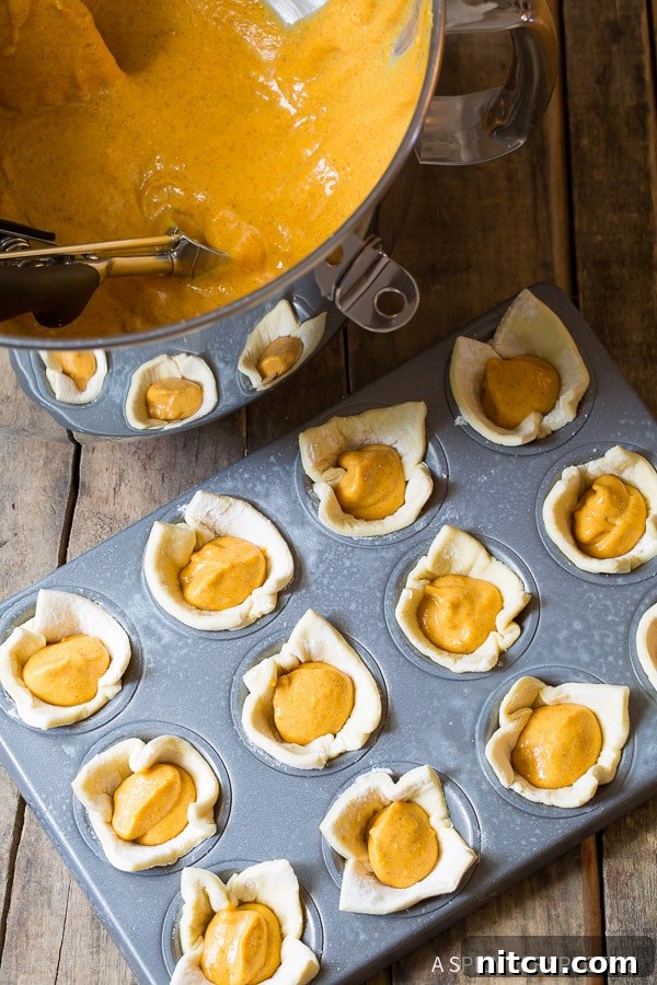 Freshly baked Mini Pumpkin Pies cooling in the pan, their golden crusts and puffed filling promising delight.