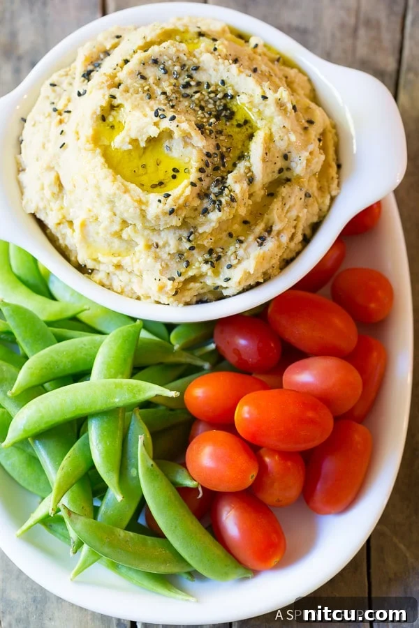 Top down view plate of fresh sweet peas and grape tomatoes snuggled around a white dish of sesame miso hummus.
