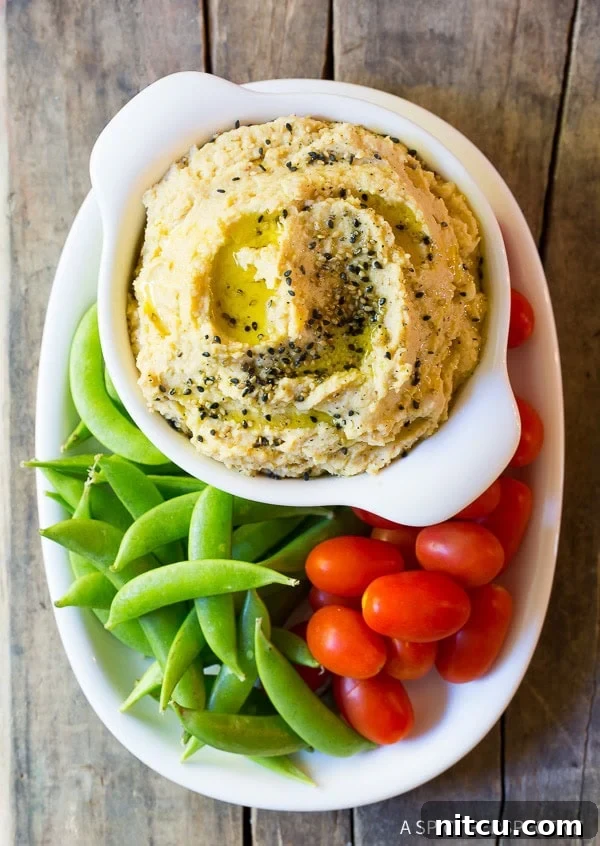 Top down view plate of fresh sweet peas and grape tomatoes snuggled around a white dish of sesame miso hummus.