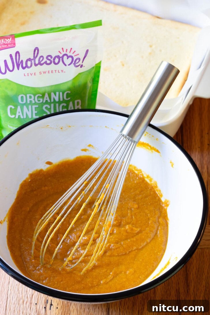 Pouring the spiced pumpkin mixture over the cooled cheesecake layer.
