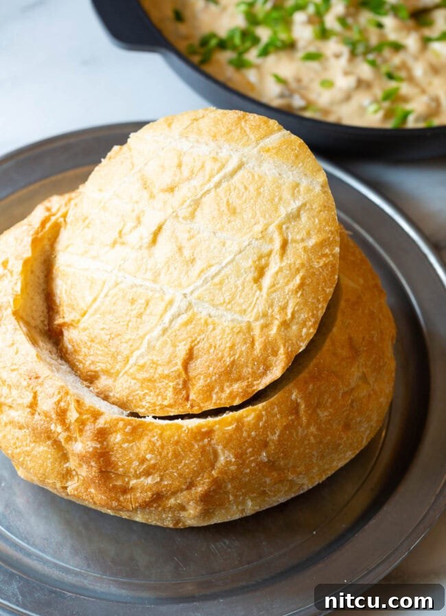 A large, perfectly prepared sourdough bread loaf with its top removed, revealing the hollowed-out center, ready to be filled with the delicious dip.