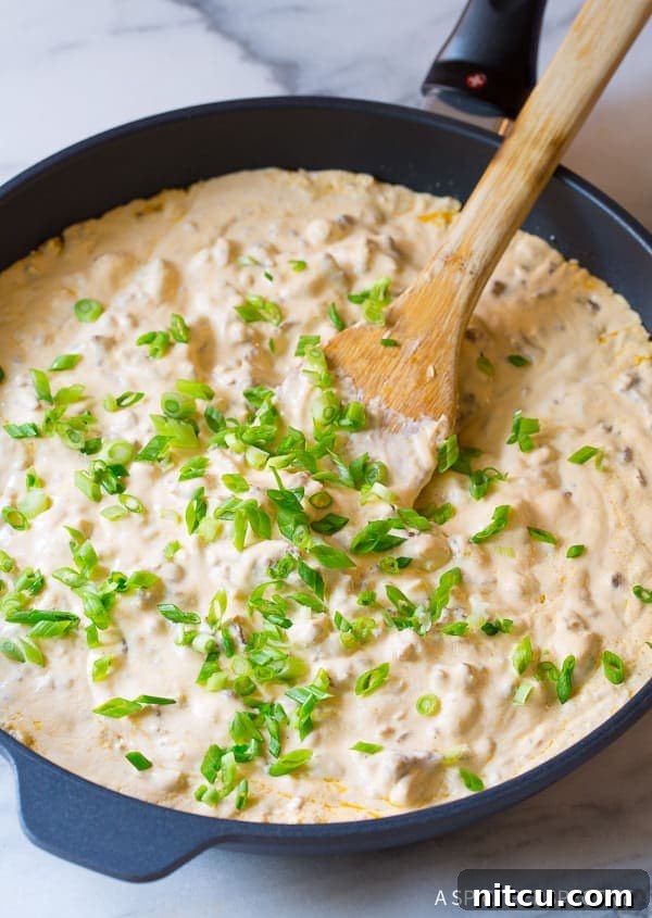 A close-up of the creamy sausage cheese dip in a skillet, beautifully garnished with fresh, vibrant green onions.