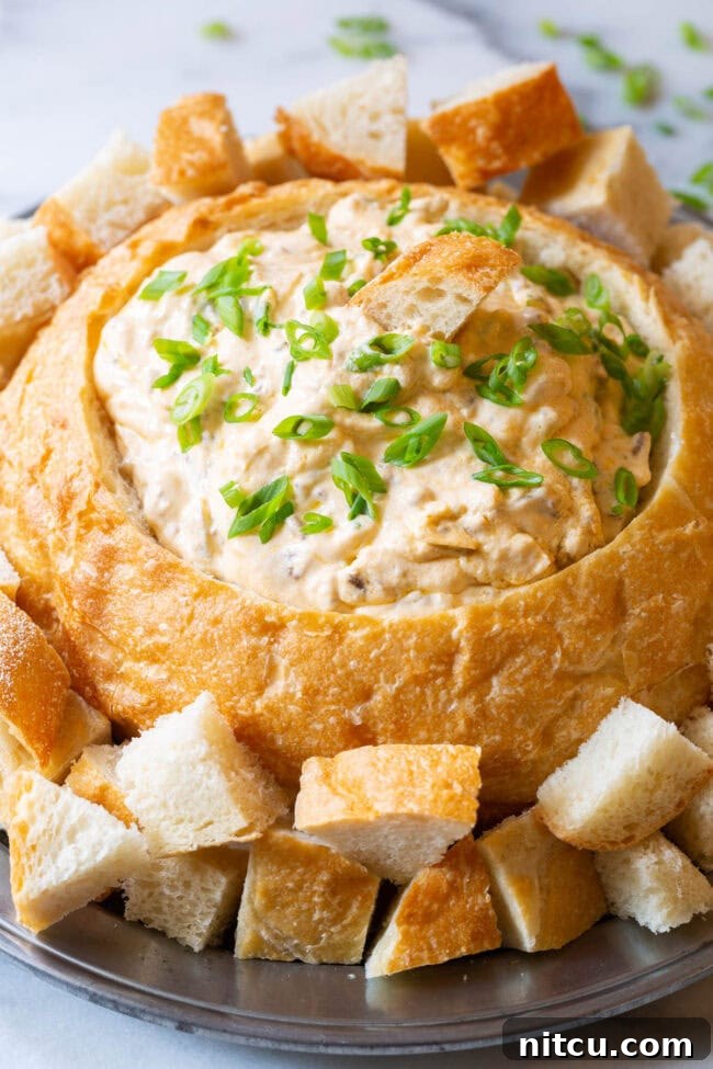A bountiful sourdough bread bowl filled with creamy sausage cheese dip, surrounded by an array of dippable bread chunks, inviting guests to enjoy.