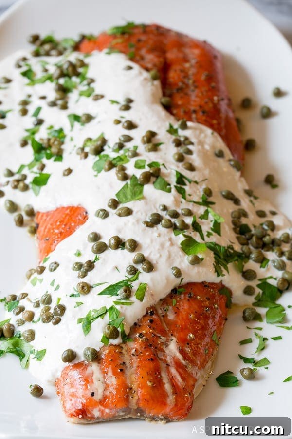 Smoky baked salmon with creamy white horseradish sauce on top, garnished with capers and fresh dill.