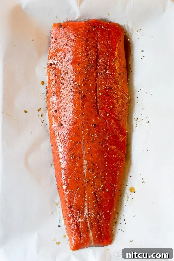Raw salmon fillet on a baking sheet lined with parchment paper, ready for seasoning.