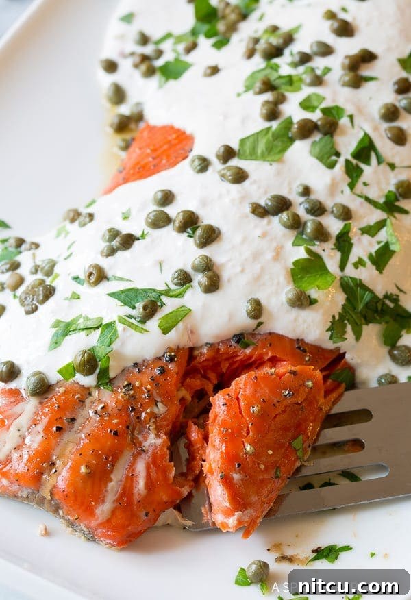 Close-up of baked salmon with horseradish sauce and capers, with a spatula gently flaking off a portion, highlighting its tender texture.