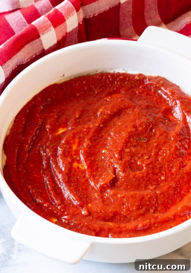 Tomato sauce spread on top of cheese in a white round baking dish.