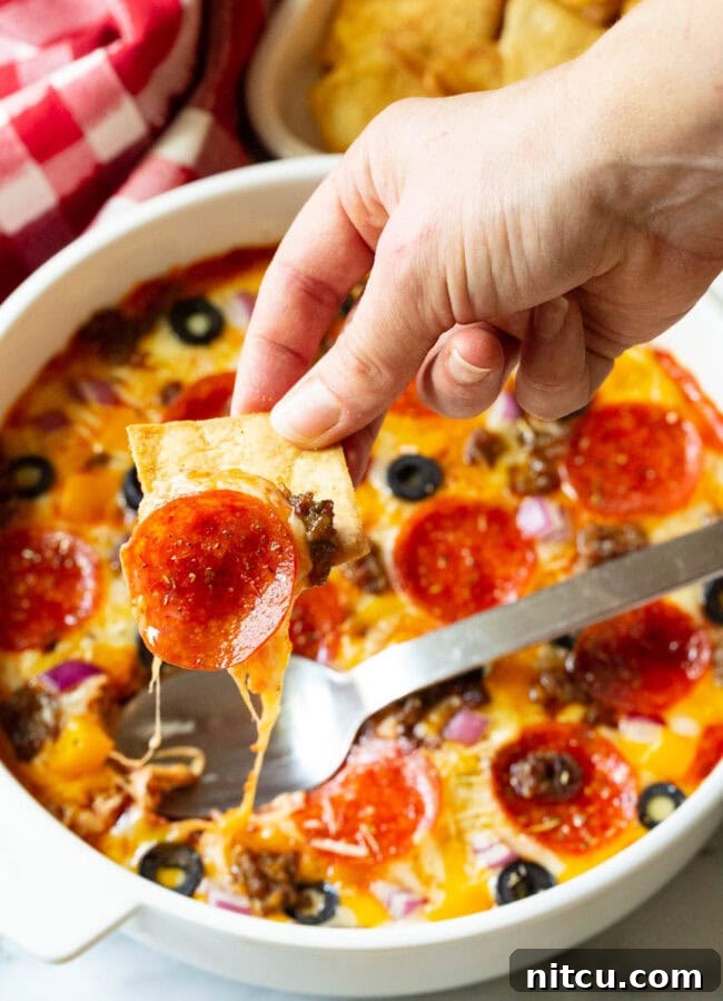Hand using a pita chip to scoop a bite of pepperoni pizza dip. 