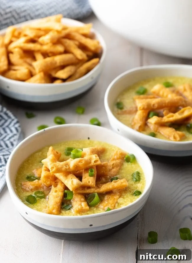 Two bowls of egg drop soup topped with crispy noodles and slice green onions.