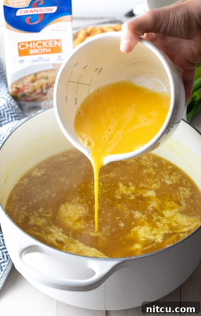 Adding whisked eggs from a white measuring bowl into a pot of broth.