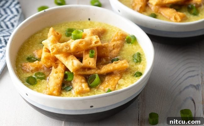 A bowl of egg drop soup topped with crispy noodles and slice green onions.