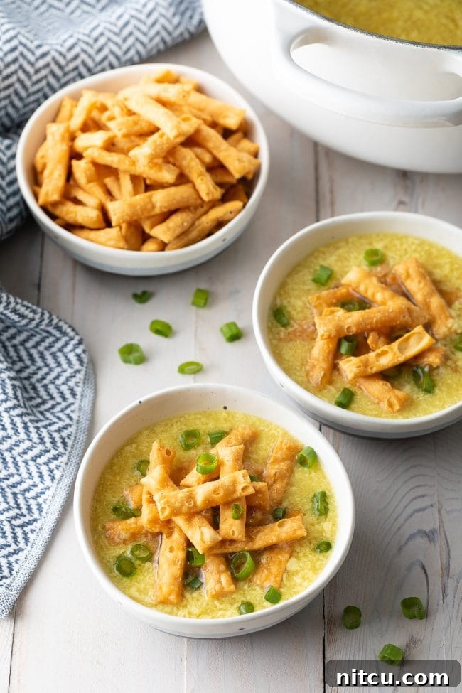 Two bowls of egg drop soup topped with crispy noodles and slice green onions.
